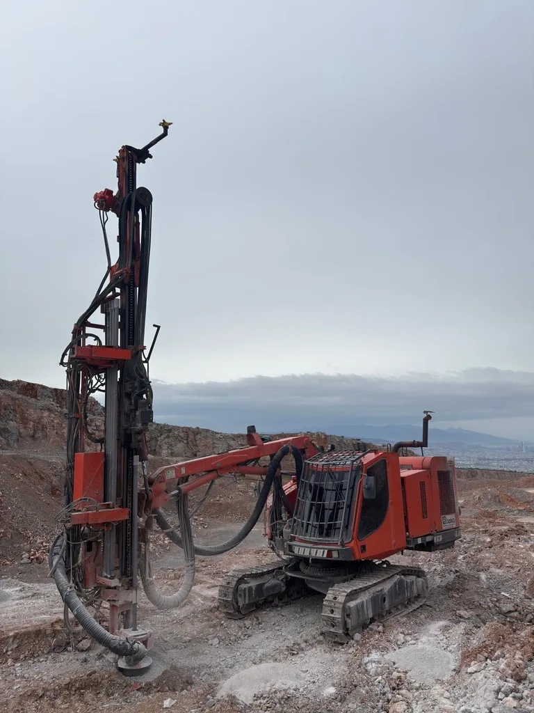 Red crawler drill rig working on a quarry bench