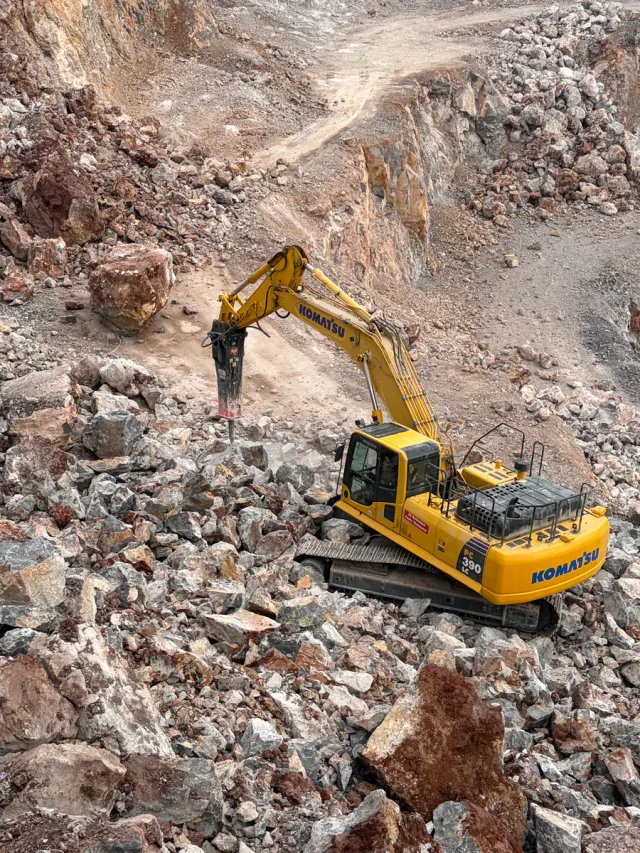 Tracked excavator breaking rock among quarry boulders